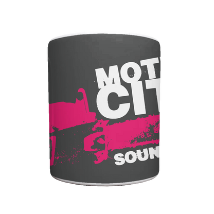 White mug with black background, MOTION CITY SOUNDTRACK in bold white lettering, pink chainsaw graphic.